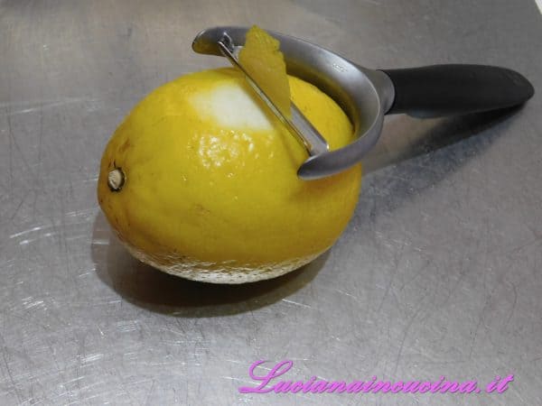 Tagliare con l'apposito attrezzo la buccia del limone, solo la parte gialla poichè quella bianca rilascia un sapore amarognolo.