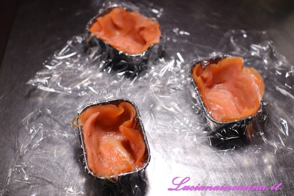 Foderare degli stampini con pellicola per alimenti poi inserire le fette di salmone ai lati e sul fondo.