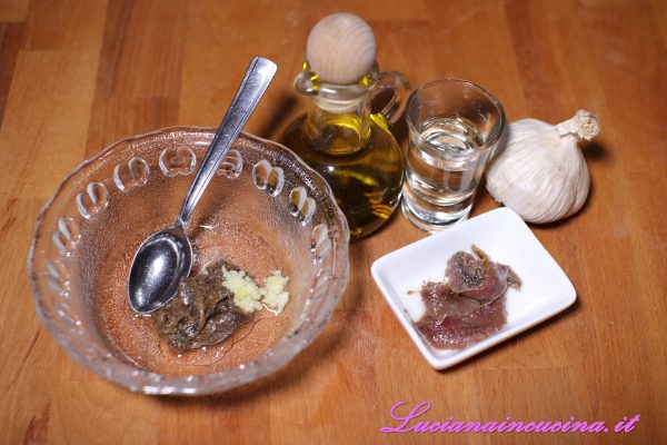 Preparare un pesto con lo spicchio d'aglio (se non lo gradite lasciatelo intero e toglietelo dopo un po'), i filetti di alici sott'olio, l'aceto bianco, sale, pepe e olio extravergine d'oliva.