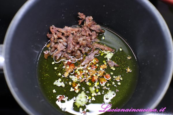 A parte in un pentolino sciogliere i filetti di alici nell'olio insieme all'aglio spremuto ed ai peperoncini sbriciolati.