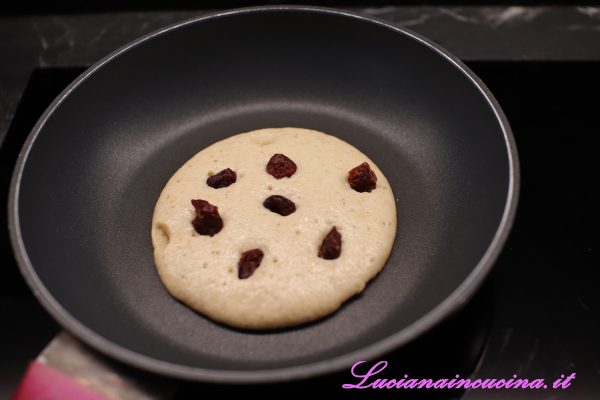 Aggiungere qualche mirtillo rosso sulla superficie del pancake e, quando si formeranno delle bollicine, girarlo e proseguire brevemente la cottura.