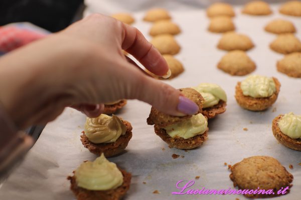 Farcire i baci con la crema incorporando un po' di granella di pistacchi tra un biscotto e l'altro.